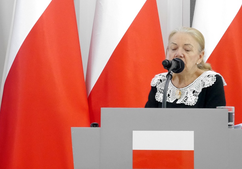 prof. Zofia Chyra-Rolicz wygłaszająca prelekcję na tle biało-czerwonych flag